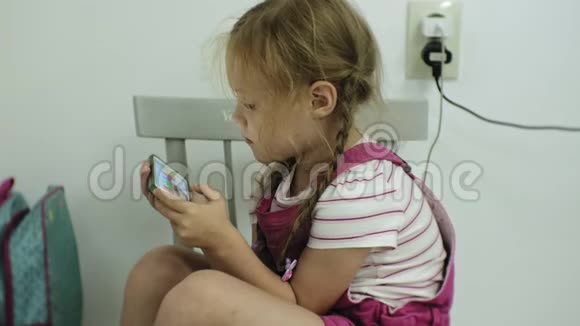坐在椅子上的小女孩试图用她的智能手机玩游戏儿童使用手机视频的预览图