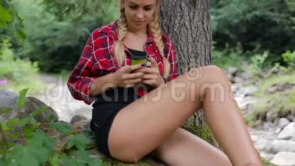 快乐女孩坐在森林里在智能手机上发短信视频的预览图
