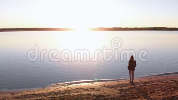 年轻女子在春天的河滩黄金时段享受日落穿着白色的裤子短汗和夹克视频的预览图
