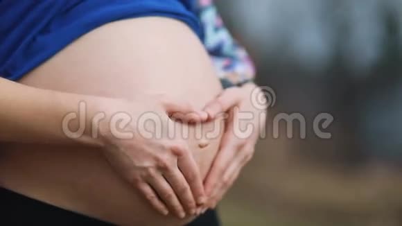 未来怀孕的母亲穿着复古的衣服抚摸着她的腹部用手指在中心创造出心形视频的预览图