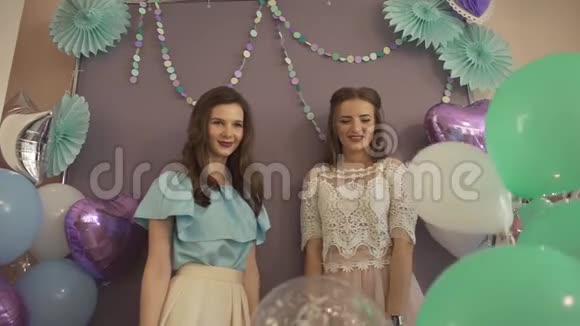 两个年轻迷人的兴奋的女人穿着漂亮的裙子带着气球扔着五彩纸屑在镜头前微笑视频的预览图