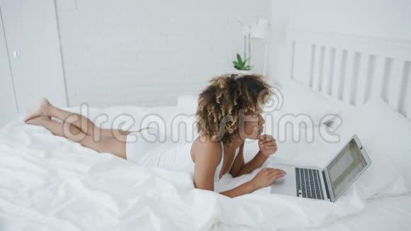 漂亮的女人躺在床上拿着笔记本电脑视频的预览图