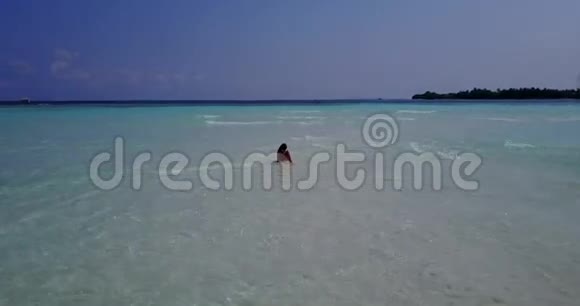 在阳光明媚的热带沙洲上一位年轻美丽的女士在沙滩上观看马尔代夫白色沙滩视频的预览图