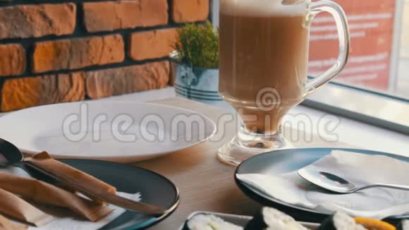 在时尚的咖啡屋里咖啡拿铁放在寿司卷旁边的透明玻璃杯里视频的预览图