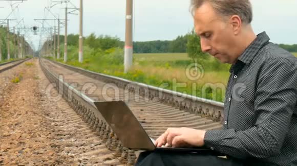 一个男人坐在铁轨上在笔记本电脑上写着一封信视频的预览图