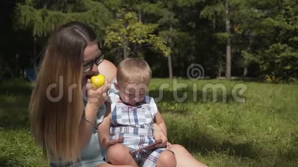 妈妈和孩子在公园野餐看着智能手机吃着苹果视频的预览图