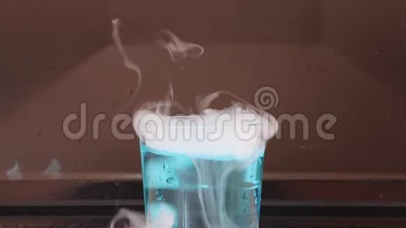干冰在一杯蓝色的水和产生白色的烟雾在黑暗的背景视频的预览图