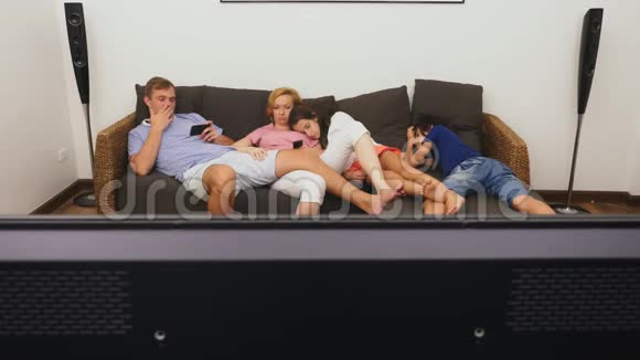 可爱的家人妈妈爸爸女儿和儿子一起在客厅里看电视在前面睡着了视频的预览图