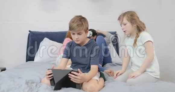 儿子使用平板电脑而父亲则在卧室戴虚拟现实眼镜一家人一起在家玩视频的预览图
