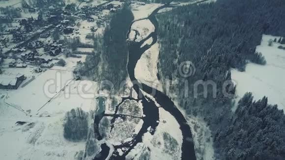 在雪地上鸟瞰森林小河和典型的东欧小镇或村庄视频的预览图