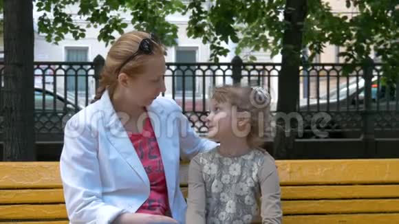 母亲和女儿坐在城市公园的长凳上说话趣轻轻拥抱视频的预览图