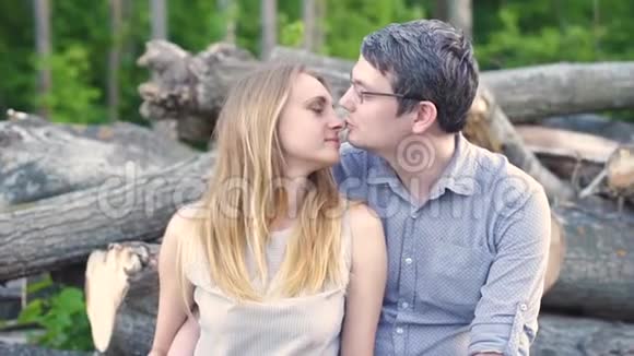 一对在森林背景下砍伐的原木上的情侣拥抱亲吻视频的预览图