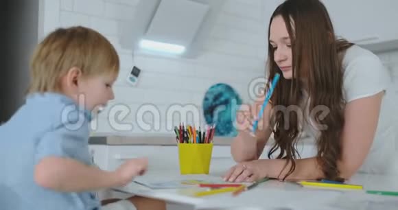 妈妈帮儿子学画做作业学前准备在家坐在白色厨房视频的预览图