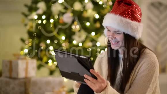 在圣诞树背景下用手中的平板电脑特写了CuteBrunette的肖像圣诞老人的情感女孩观视频的预览图