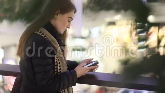 在shoppng购物中心一个身材魁梧的乌克兰女孩用智能手机和她的朋友聊天在前面的计划上没有重点的叶子视频的预览图