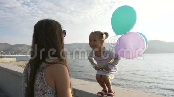 可爱的小女孩从人行道上跳到她的年轻母亲在海边的手上视频的预览图
