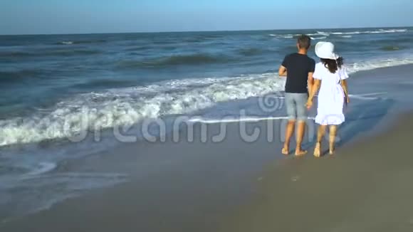 一对年轻夫妇正沿着海滨散步他们相爱牵手晴朗阳光明媚的一天一个女孩视频的预览图