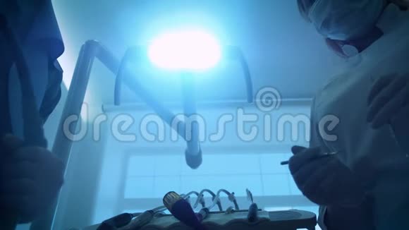 戴面具的两位牙医医生微笑着手里拿着口镜和钩子打开了牙科灯的灯视频的预览图