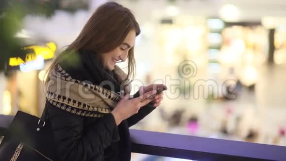 微笑着迷人的阳光模特微笑着在购物中心的露台上敲击电话稳定的凸轮缓慢的视频的预览图