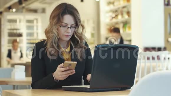 商务女性同时在笔记本电脑和智能手机上工作穿着商务服的妇女在非正式场合工作视频的预览图