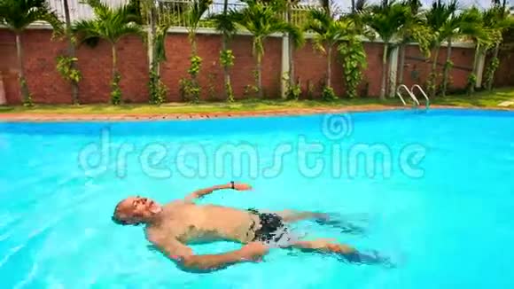大胡子老人沿着椭圆形游泳池游回来视频的预览图