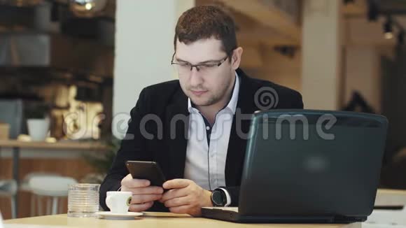 穿着商务服的人在咖啡馆里用笔记本电脑和手机工作视频的预览图