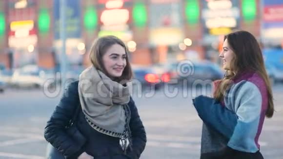 两个年轻迷人的女孩在巨大的建筑前的城市街道上笑着稳定凸轮缓慢移动视频的预览图