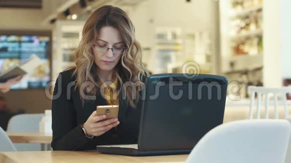 商务女性同时在笔记本电脑和智能手机上工作穿着商务服的妇女在非正式场合工作视频的预览图