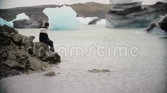 年轻的帅哥坐在冰泻湖的岩石上欣赏风景独自探索冰岛的男性视频的预览图