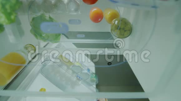 一个年轻的女人把食物装在冰箱里打开冰箱的门放在那里刚买的蔬菜视频的预览图