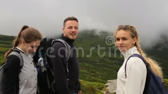 一个男人和两个旅行的女孩在山和雾的背景下看着相机视频的预览图