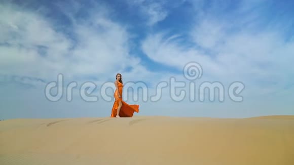 女孩在巴克汉的沙漠里散步穿着裙子的女人在阳光下的沙漠中的沙丘上行走风吹乱了她的头发视频的预览图