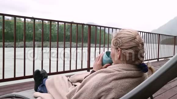 年轻女子在河边喝热咖啡或茶在山区度假胜地平静舒适的时光视频的预览图