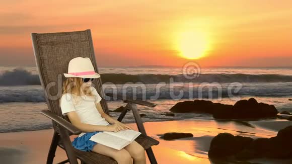 年轻的白种人女孩坐在扶手椅上看书橙色日落海平线海岸线海滩同样的夹子视频的预览图