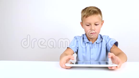 年轻英俊的金发男孩穿着蓝色衬衫用平板电脑视频的预览图