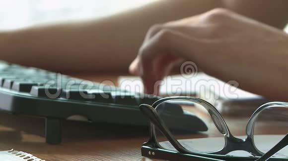 男人的双手放在键盘上在电脑旁工作桌子旁边放着眼镜有记录的文件视频的预览图