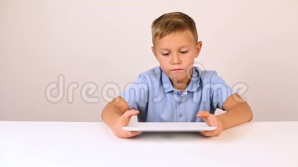 年轻英俊的金发男孩穿着蓝色衬衫用平板电脑视频的预览图