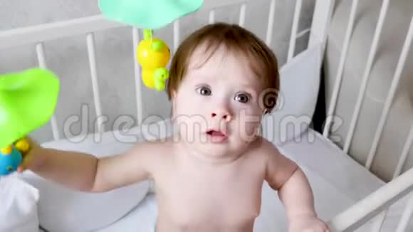 穿着尿布的小孩子拿着玩具和玩具站在婴儿床上视频的预览图