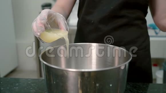 在厨房里女人把一种黄色的液体从玻璃杯里倒入平底锅里视频的预览图