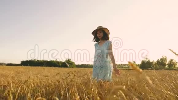 日落时分戴着草帽穿着裙子穿过金色麦田的女孩视频的预览图