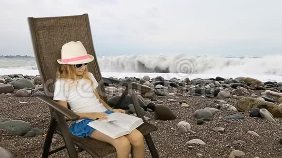年轻的白种人女孩坐在扶手椅上看书海底背景和卵石前景有过视频的预览图