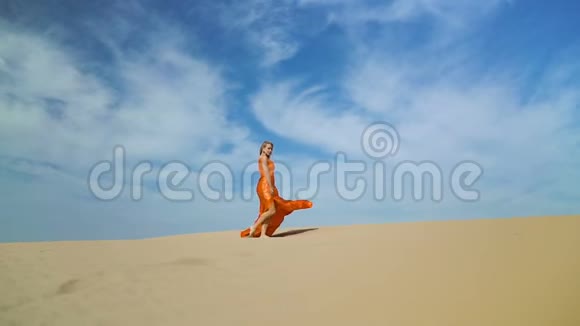 女人在沙丘上的沙漠中行走金发姑娘在烈日下的沙漠中的巴克汉散步风吹乱了她的头发视频的预览图