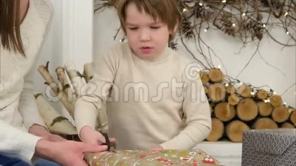 一个严肃的小男孩帮他妈妈剪圣诞礼物的包装纸视频的预览图