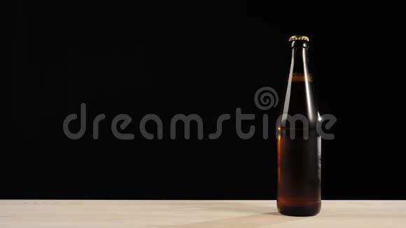 新鲜啤酒手把一个绿色的瓶子和美味的工艺啤酒放在棕色瓶子附近啤酒放在木桌上视频的预览图