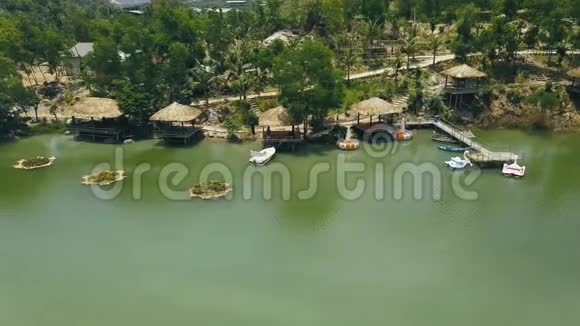 木制平房与茅草屋顶和船码头在海岸绿湖度假酒店无人驾驶飞机视图岸上的小屋视频的预览图