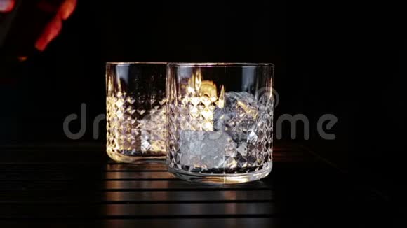 巴曼把威士忌倒在两个玻璃杯里木桌上放冰块背景黑黑重点放在冰块上视频的预览图