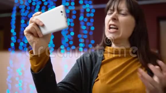 一位女性博主在室内使用蓝色电灯旁边的手机视频的预览图
