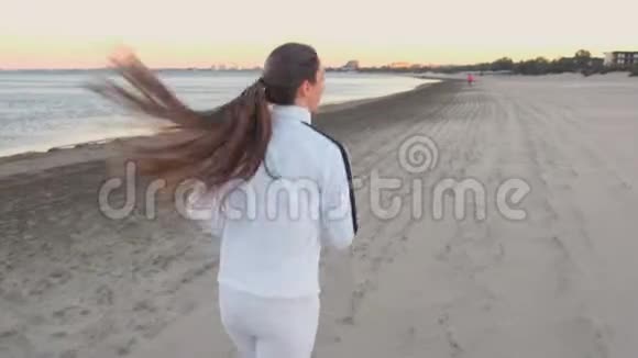 秋日日出时年轻女子正在海边的沙滩上慢跑后景视频的预览图