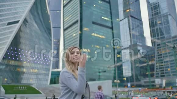 这个金发女孩在摩天大楼和城市高层建筑的背景下向相机发送一个空中吻视频的预览图