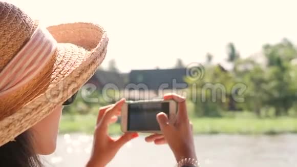 旅游女孩在大帽子拍照使用手机和游轮在泰国的河流4K慢运动视频的预览图